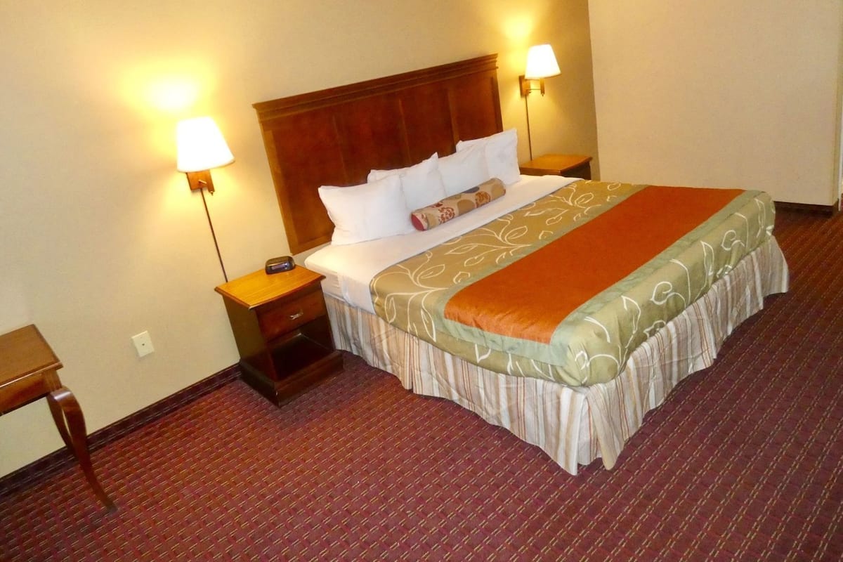A hotel room with a large bed, two bedside lamps, a wooden headboard, and a carpeted floor.