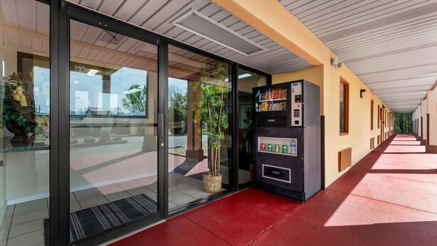 A hallway with a vending machine, glass doors, and a red floor. - Americas Best Value Inn Montezuma (Montezuma)