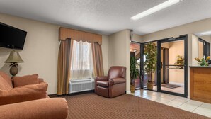 A living room with a brown leather sofa, a brown armchair, and a flat-screen TV on a stand. - Americas Best Value Inn Montezuma (Montezuma)