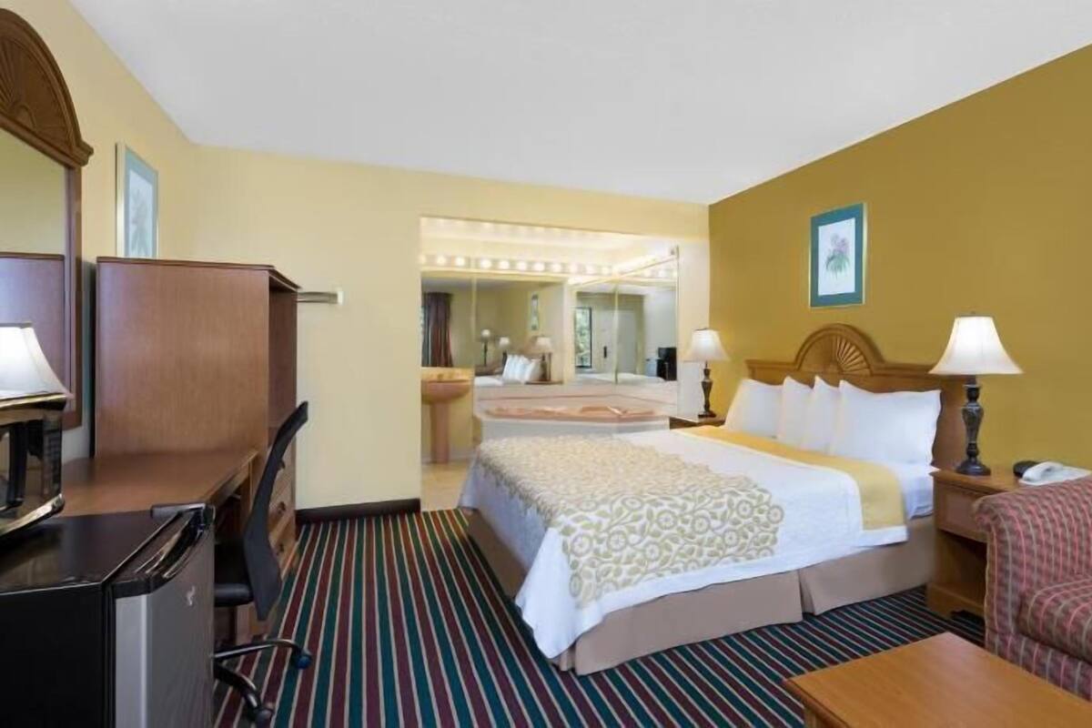 Quarto de hotel com cama, escrivaninha, cadeira, sofá e espelho.