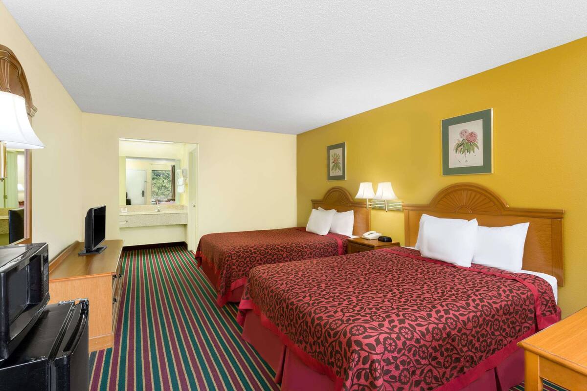 Quarto de hotel com duas camas, televisão, secretária e espelho.