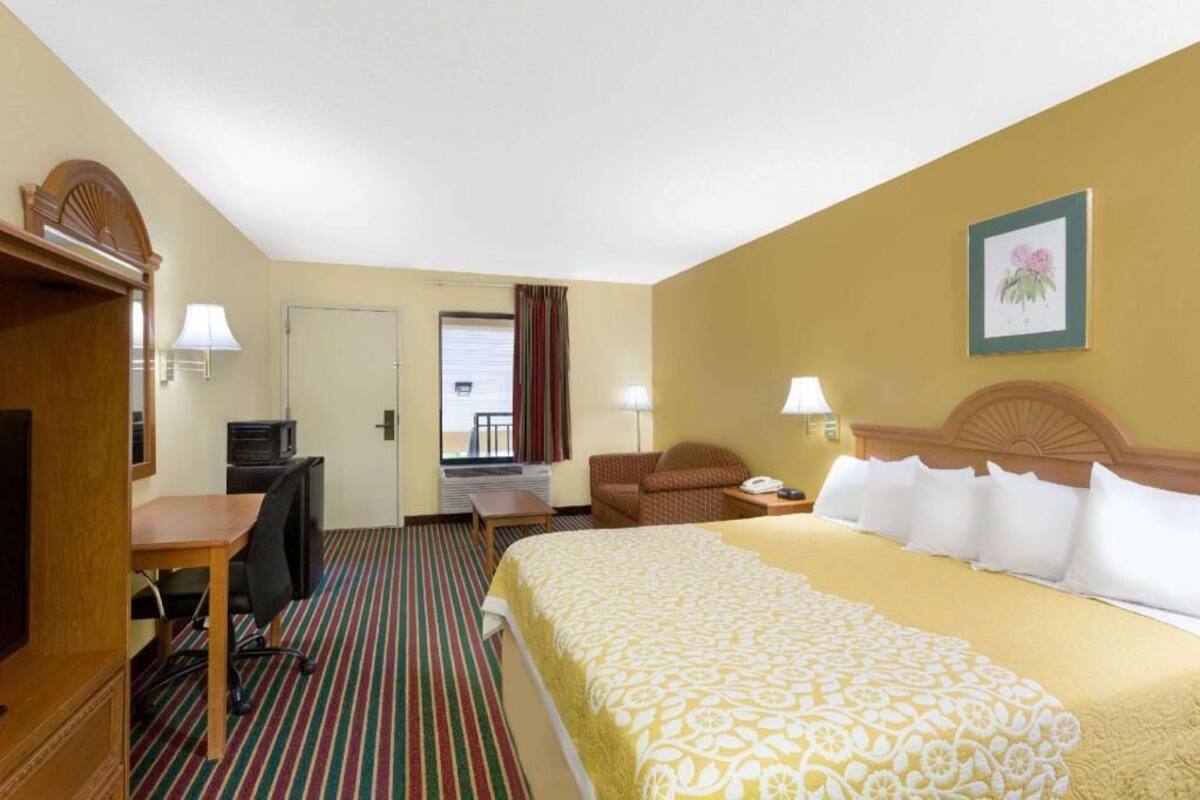Quarto de hotel com cama, escrivaninha, cadeira e televisão.