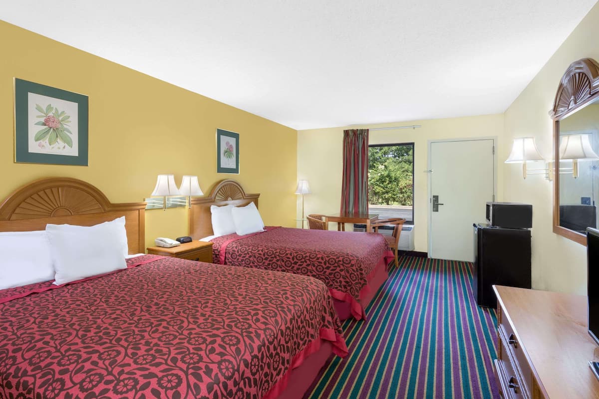 Quarto de hotel com duas camas, uma escrivaninha, uma cadeira, uma televisão e uma porta que dá para o exterior.