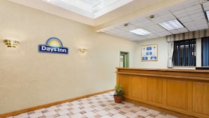A reception area with a Days Inn sign, a wooden reception desk, a potted plant, and a bulletin board with information. - Days Inn by Wyndham Biscoe (Biscoe)