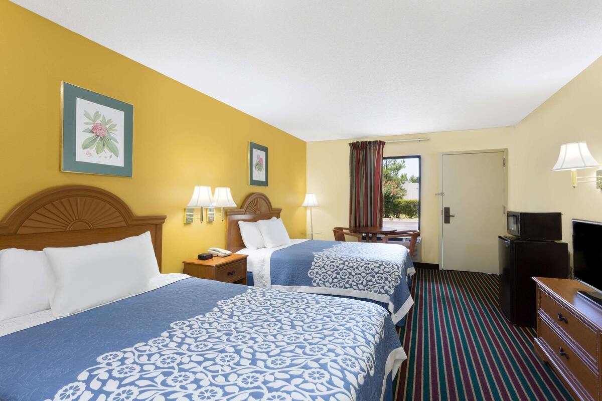 Quarto de hotel com duas camas, televisão, frigorífico e janela com cortinas.