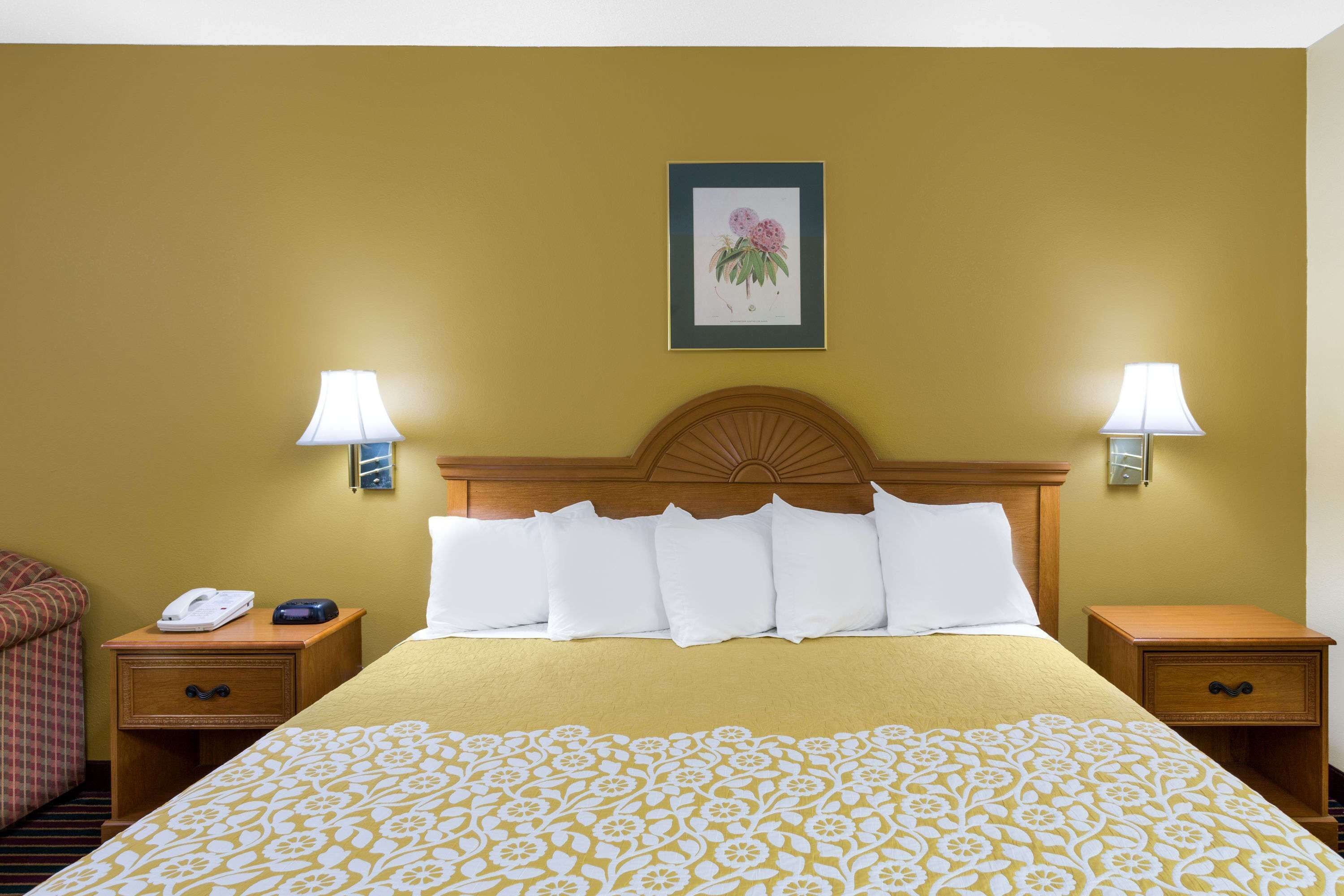 A hotel room with a large bed, two bedside tables with lamps, a wooden headboard, and a framed picture on the wall.