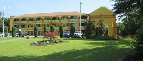 Un motel à plusieurs étages, avec une façade jaune, des balcons verts et une pelouse bien entretenue.