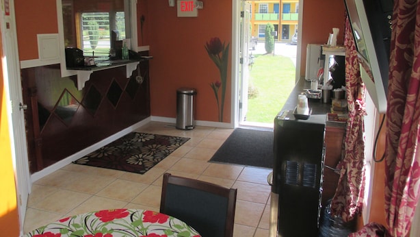 A hotel lobby with a reception desk, a trash can, a small table with chairs, and a door leading outside.