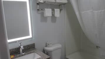 A bathroom with a granite countertop sink, a toilet, a shower with a curtain, and a towel rack with towels.