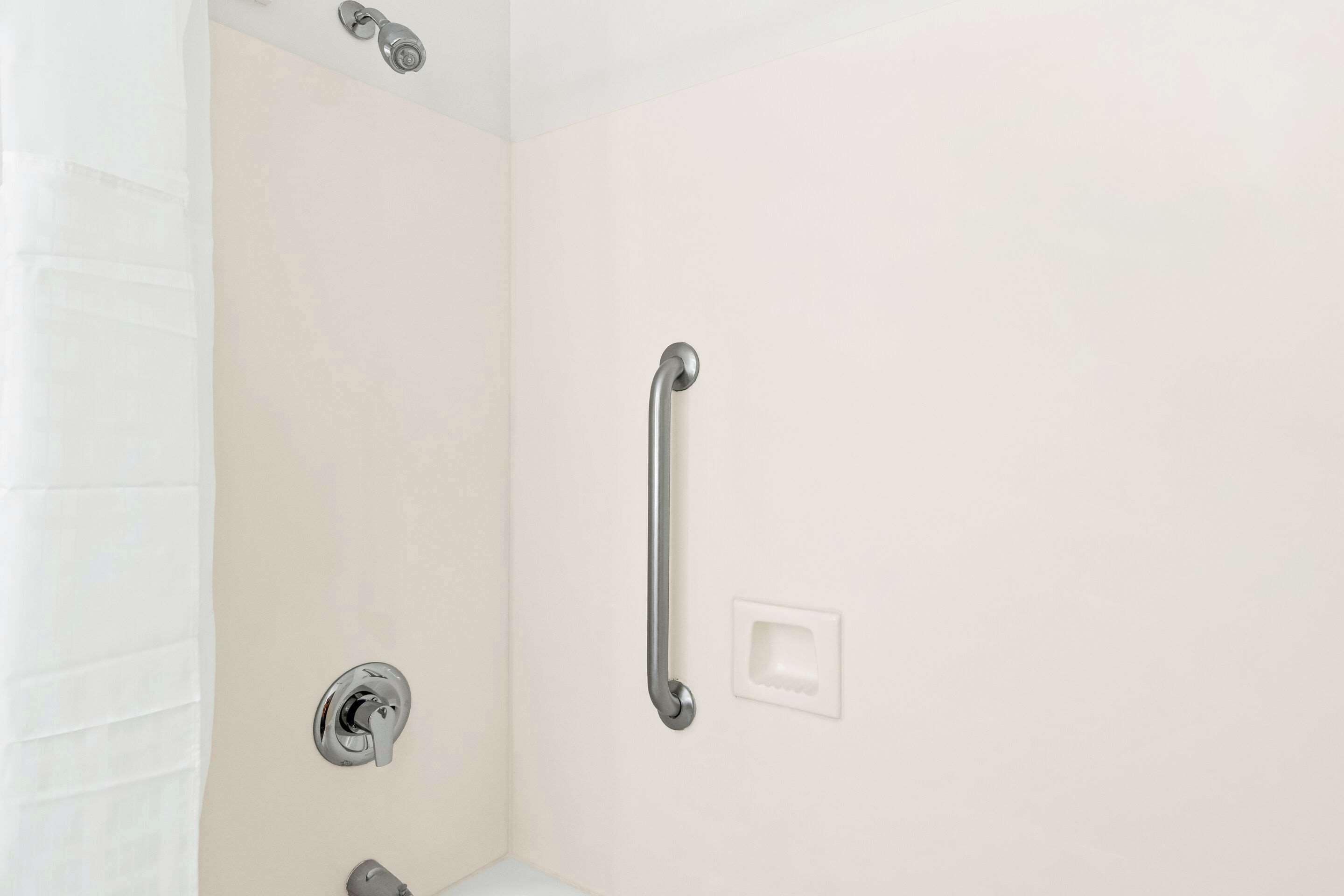 A shower area with a grab bar, a showerhead, and a control knob.