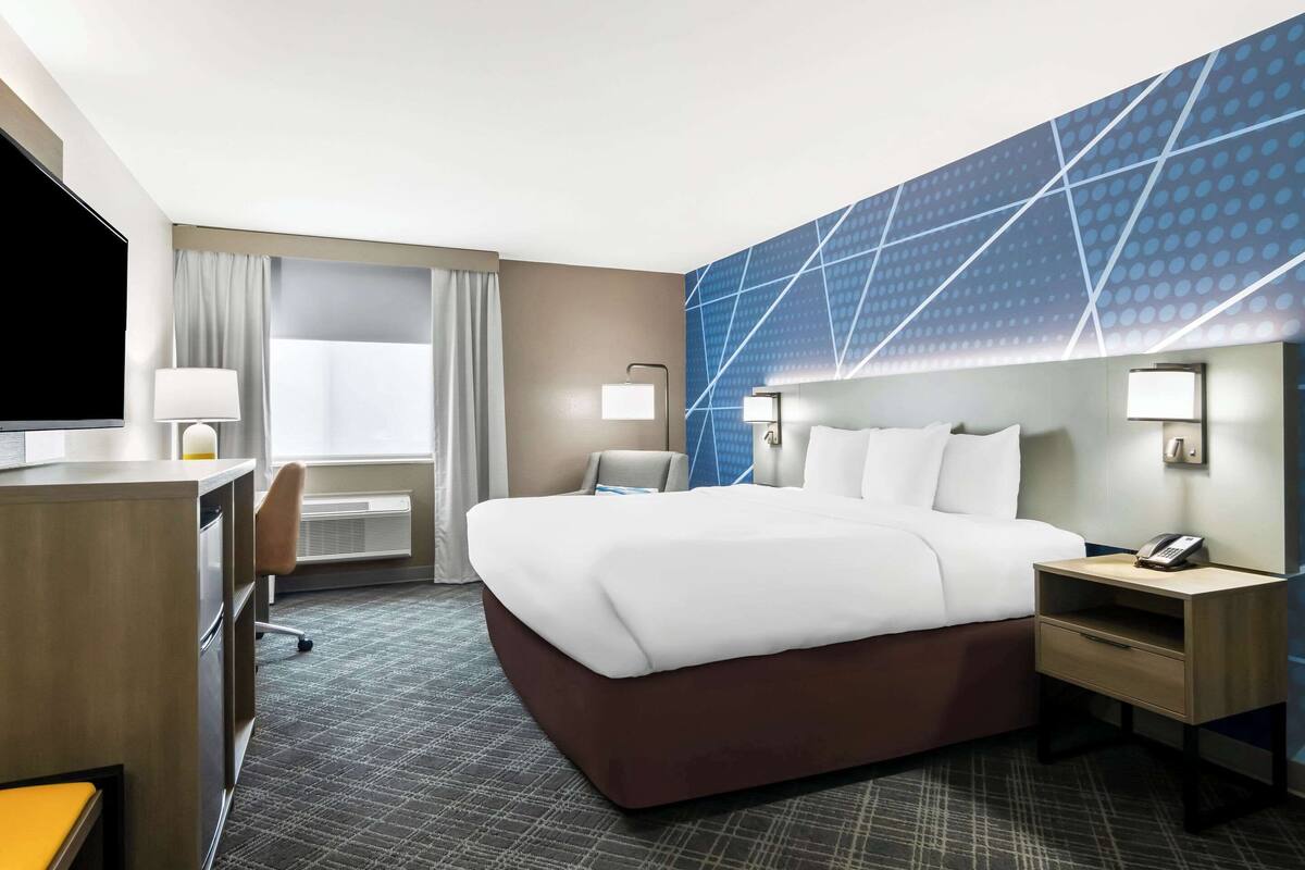 A hotel room with a large bed, a desk with a chair, a TV, and a window with curtains.