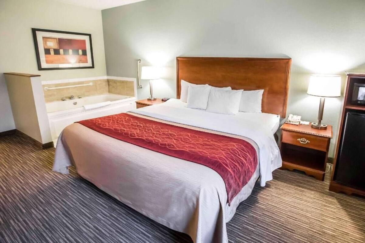 A hotel room with a large bed, a separate bathroom with a bathtub, and a small TV on a wooden nightstand.