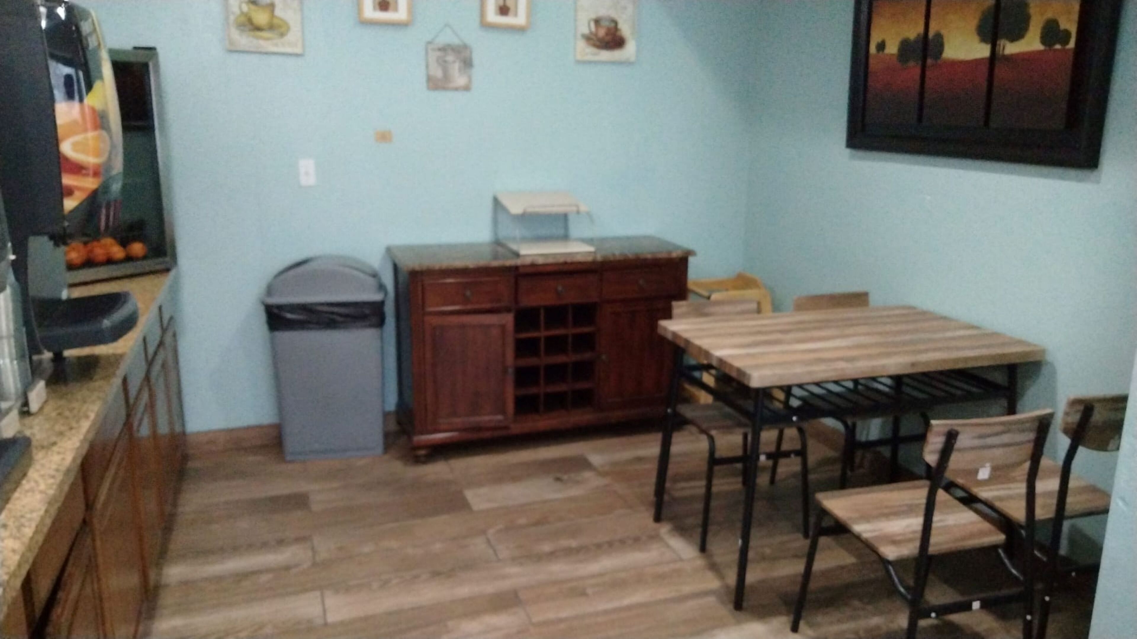 A small kitchen with a wooden table and chairs, a trash bin, and a cabinet.