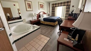 Habitación de hotel con una bañera grande, una cama doble, un escritorio con lámpara y una cafetera.