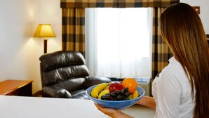 Una persona sosteniendo un cuenco de fruta en una habitación con una butaca de cuero, una lámpara y un ventanal con cortinas.