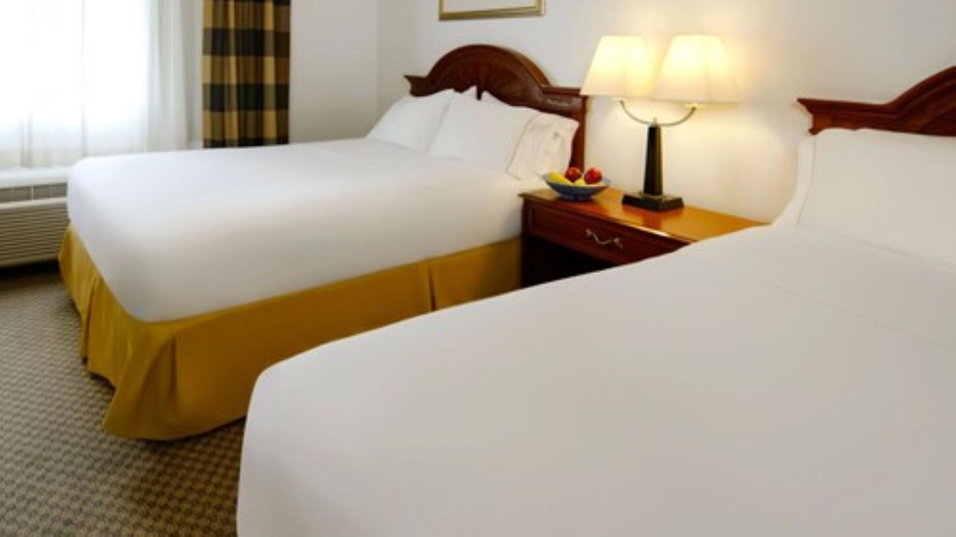 Een hotelkamer met twee bedden, een nachtkastje met een lamp en een schaal fruit.