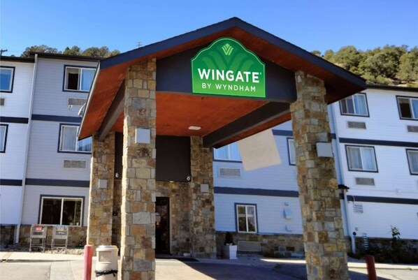 Entrada a un hotel Wingate by Wyndham con fachada de piedra y un letrero verde.