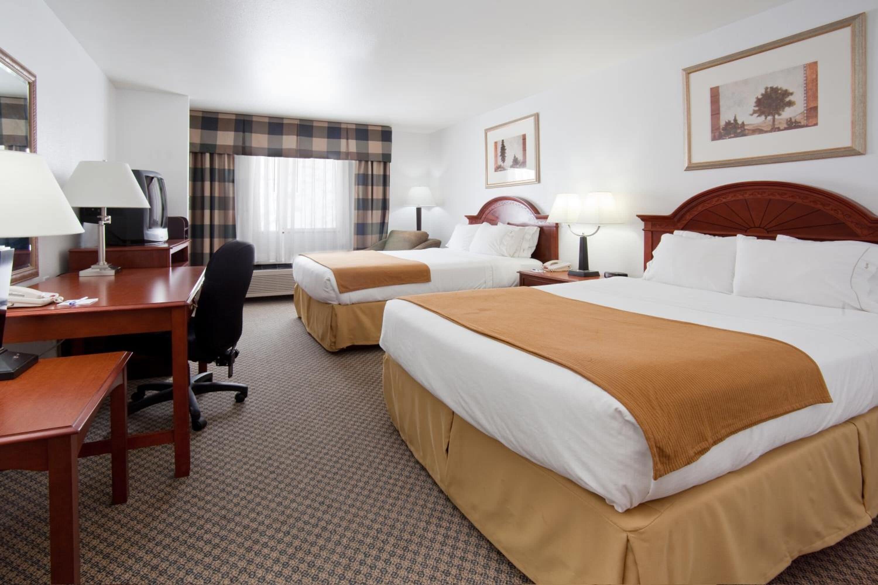 A hotel room with two beds, a desk with a chair, a television, and a window with curtains.