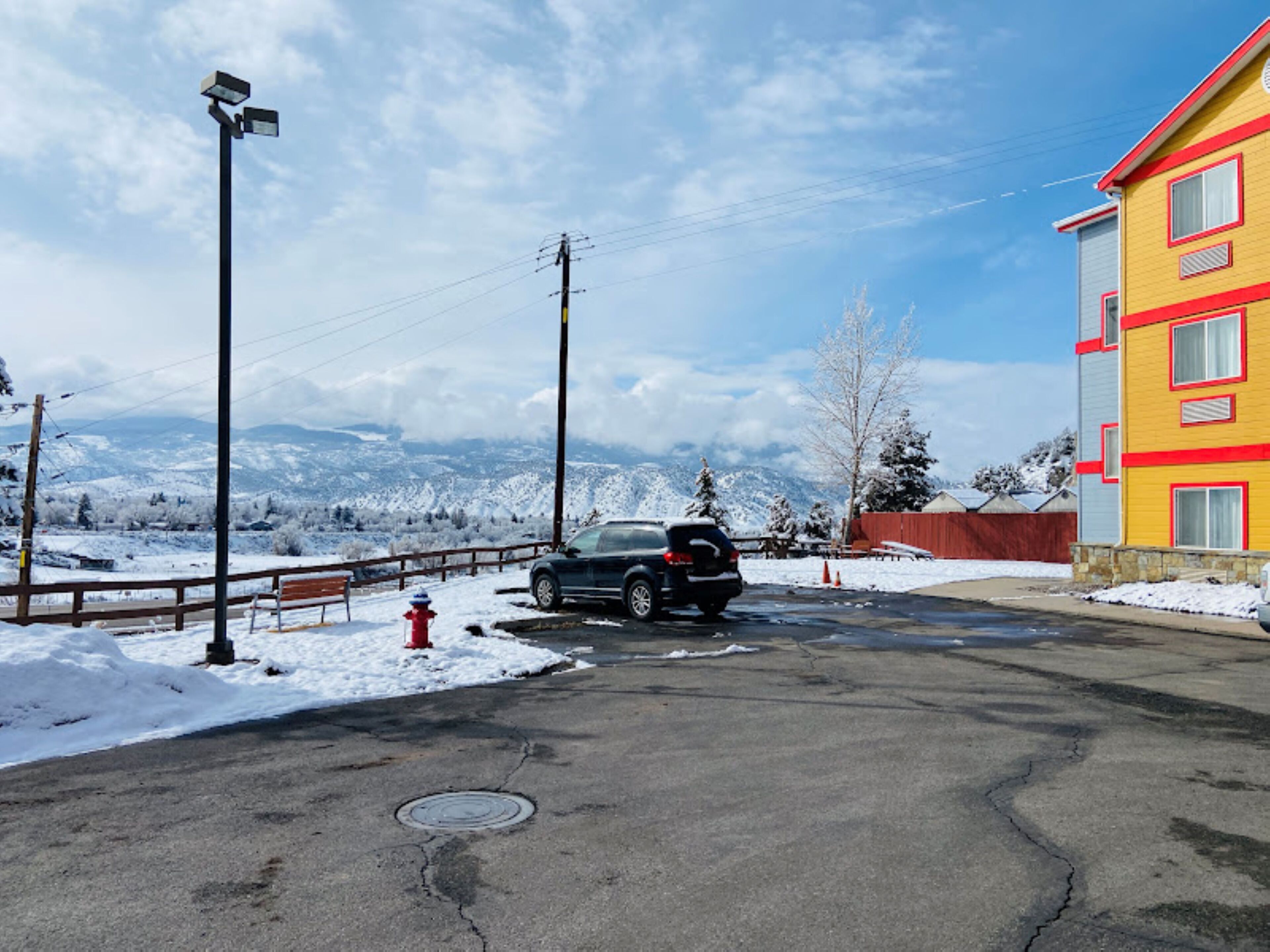 A parking lot with a snow-covered landscape, a building with red trim, and a clear sky.