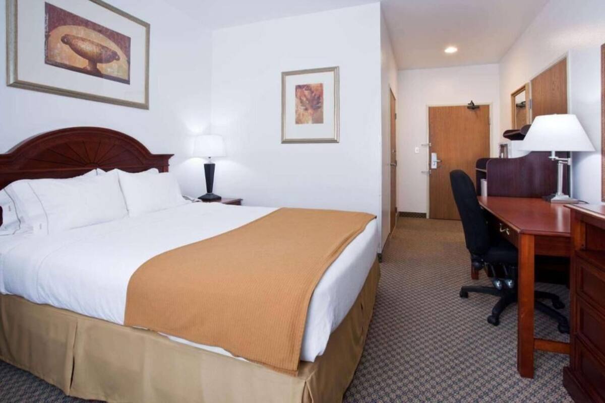 Ett hotellrum med en säng, ett skrivbord, en stol, en lampa och konstverk på väggarna.