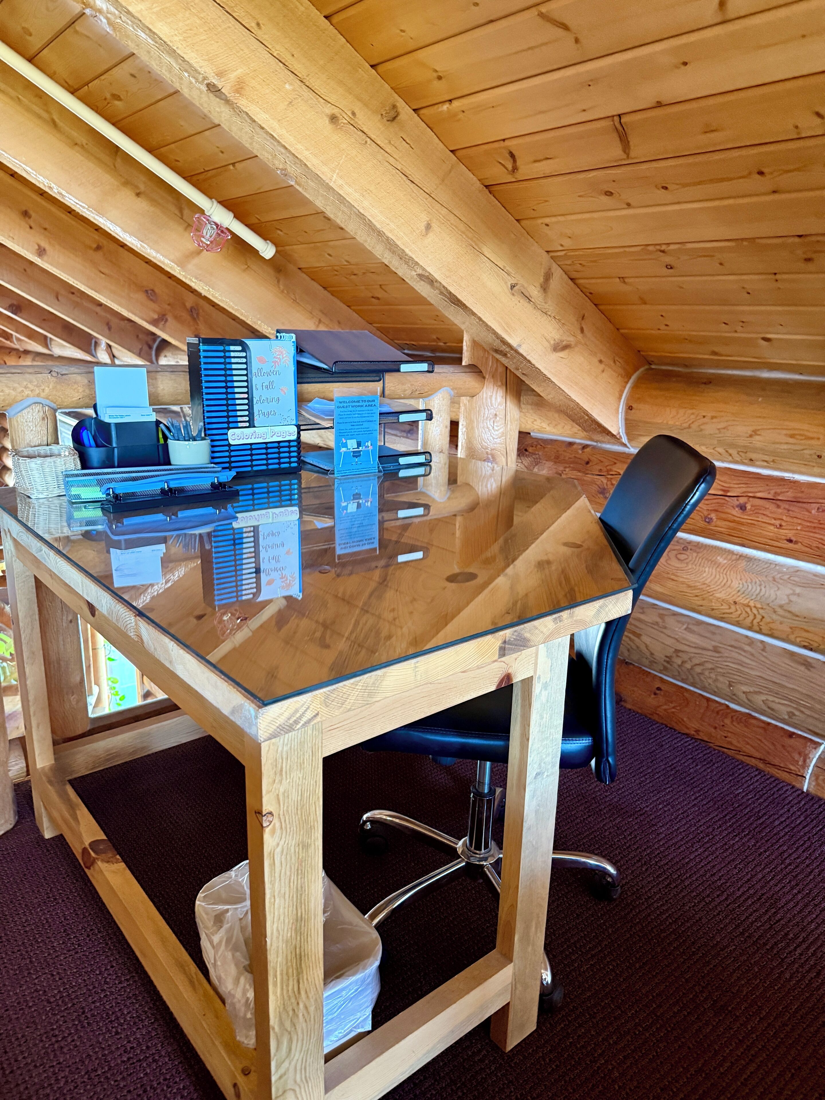 A wooden cabin with a glass-top table, black office chair, and various office supplies.