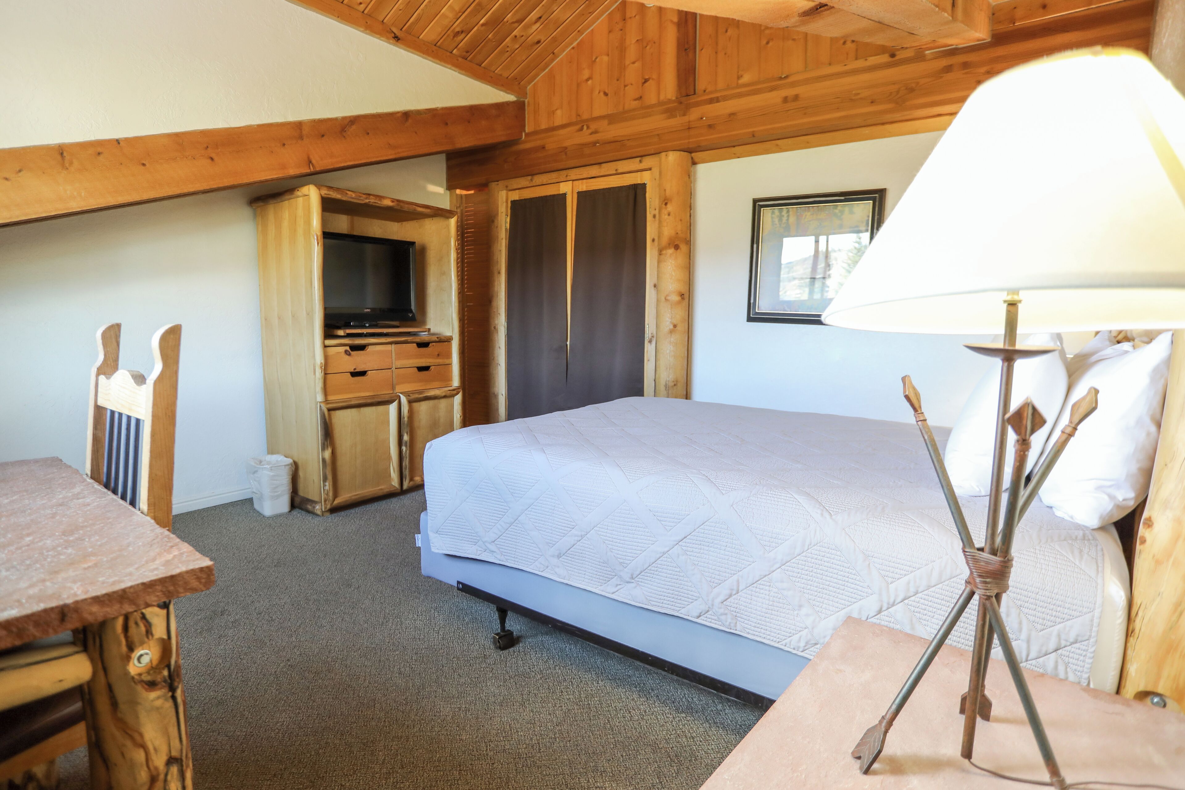 Una habitación de madera con una cama, un escritorio, un televisor y una lámpara.