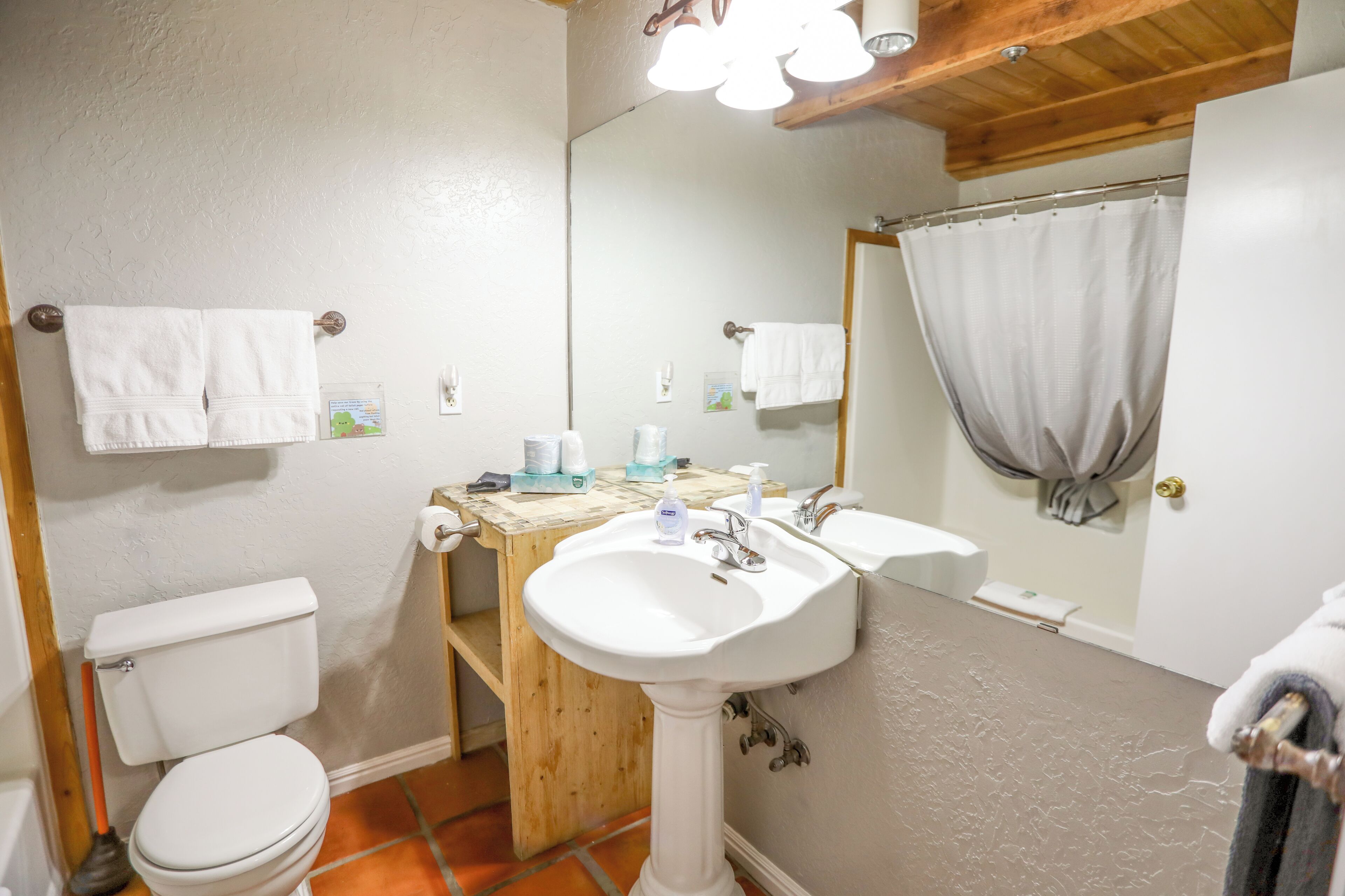 Baño con inodoro, lavamanos sobre pedestal y espejo.