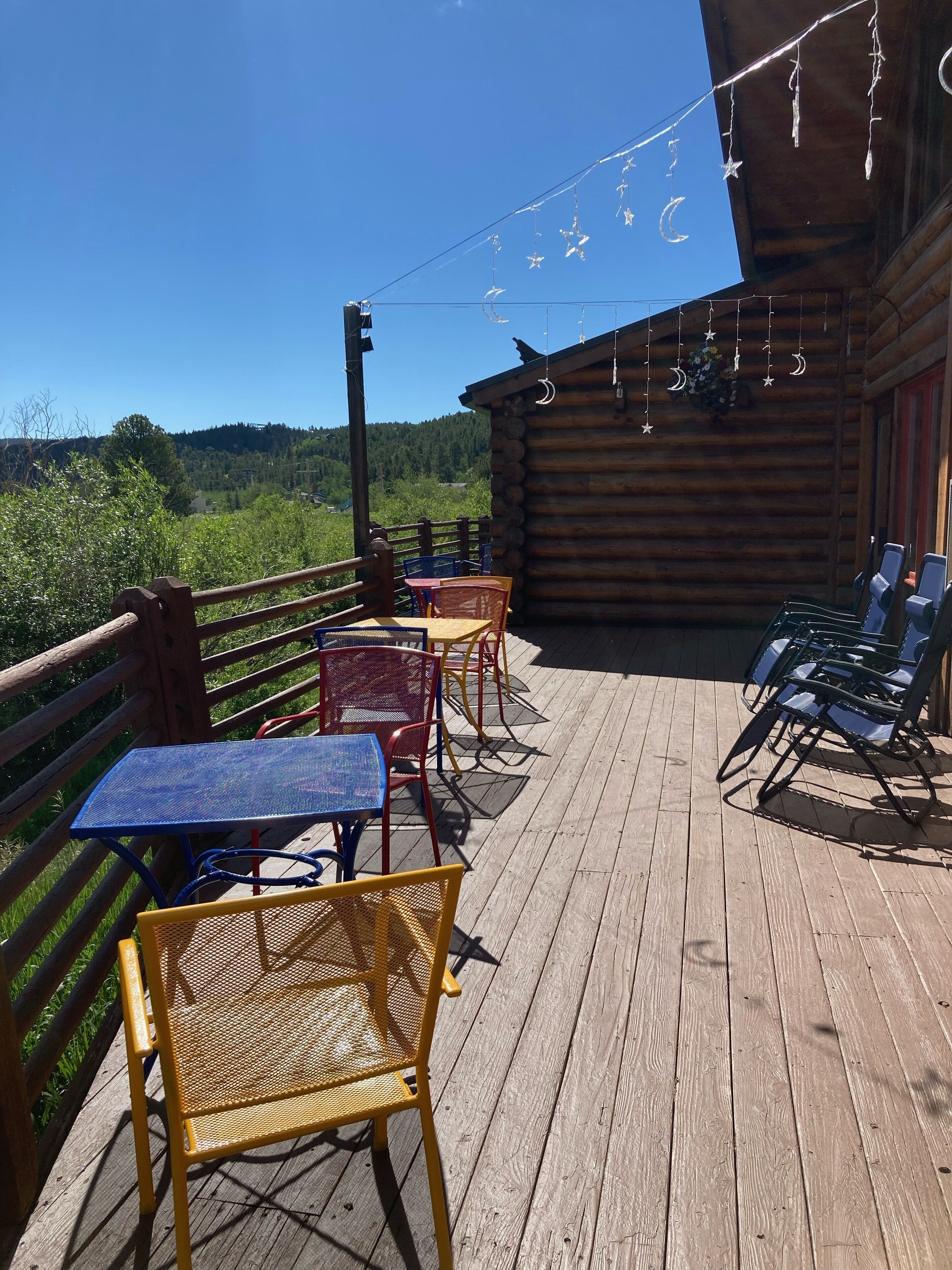A wooden deck with outdoor seating, including tables and chairs, overlooking a mountainous landscape.