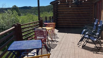 A wooden deck with outdoor seating, including tables and chairs, overlooking a mountainous landscape.