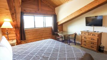A wooden cabin room with a bed, a desk, a television, and a dresser.