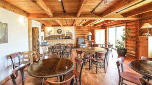 A rustic wooden interior with multiple dining tables and chairs, a kitchen area, and a large window allowing natural light. - The Boulder Creek Lodge (Nederland)