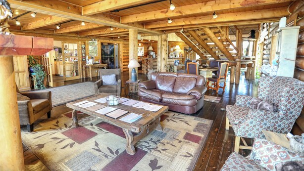 A spacious log cabin interior with a wooden ceiling, a central seating area with a coffee table, and a staircase leading to an upper level. - The Boulder Creek Lodge (Nederland)