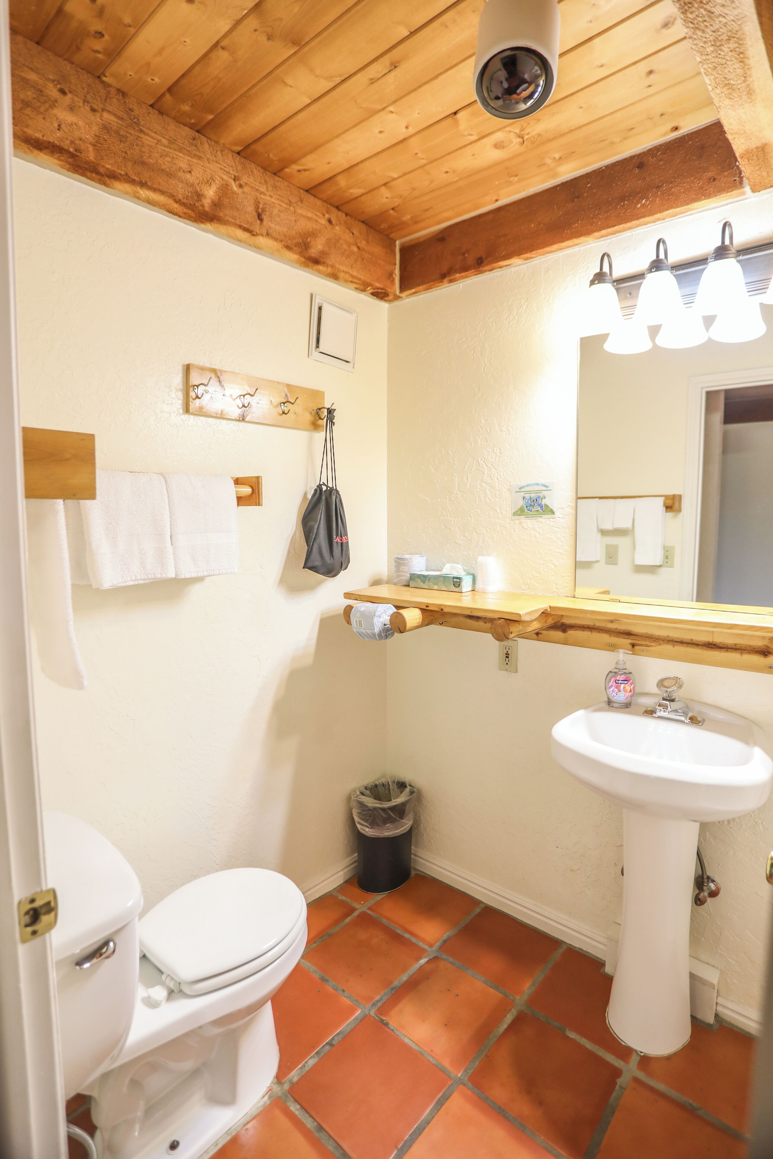 A bathroom with a wooden ceiling, white tiles, a white sink, and a toilet.