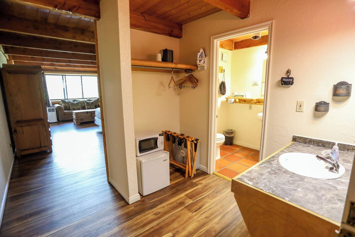 A compact kitchen with a microwave, refrigerator, and wooden fan. A small sink with a faucet and a mirror is visible.
