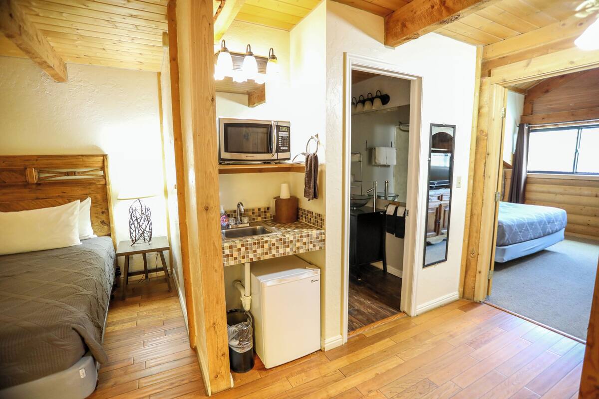 A compact room with a bed, a small kitchenette with a microwave, a refrigerator, and a sink.