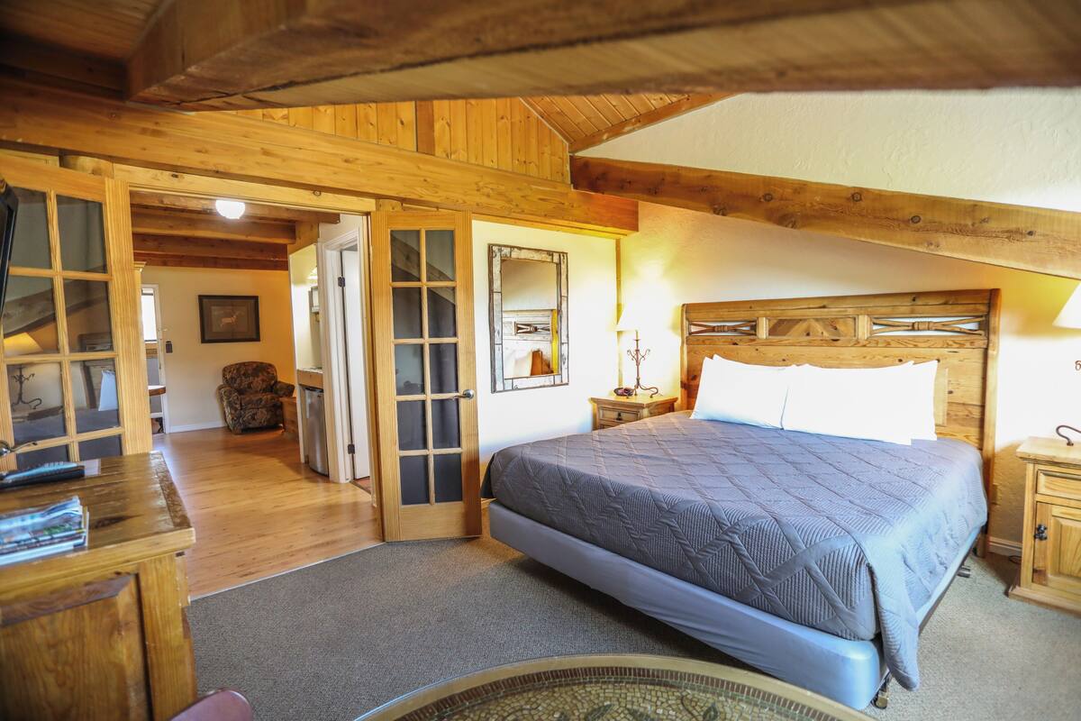 A bedroom with a large bed, wooden walls, a wooden desk, and a chair.
