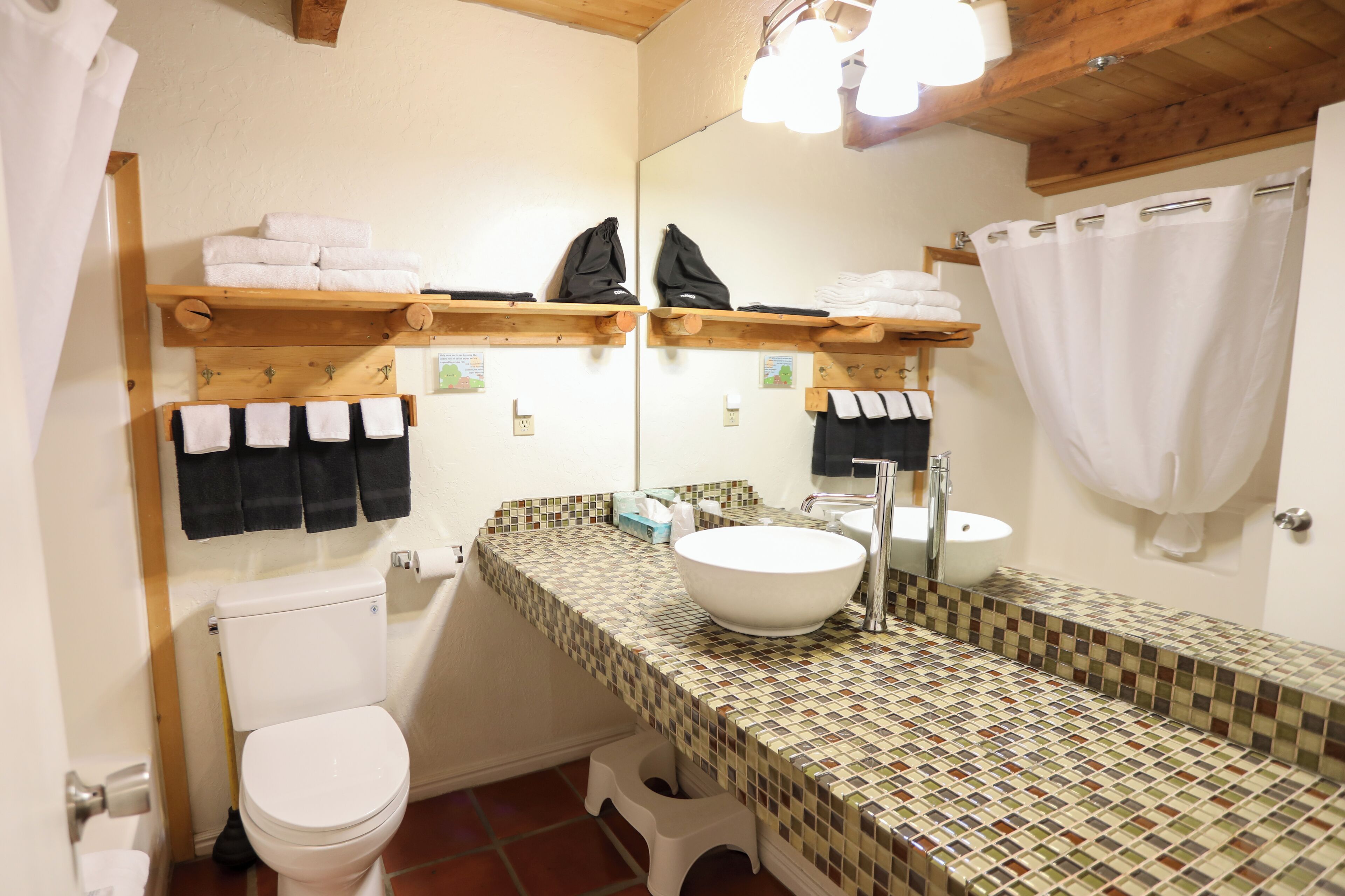 A bathroom with a white toilet, a sink with a mirror, and shelves with towels.