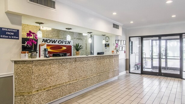 A reception area with a 'NOW OPEN' sign, a breakfast sign, a clock, and a large glass door leading outside. - Econo Lodge Darien (Darien)