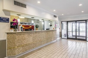 Zona de recepción con un letrero que dice 'ABIERTO' y un anuncio de desayuno, un reloj y un gran ventanal que da al exterior.