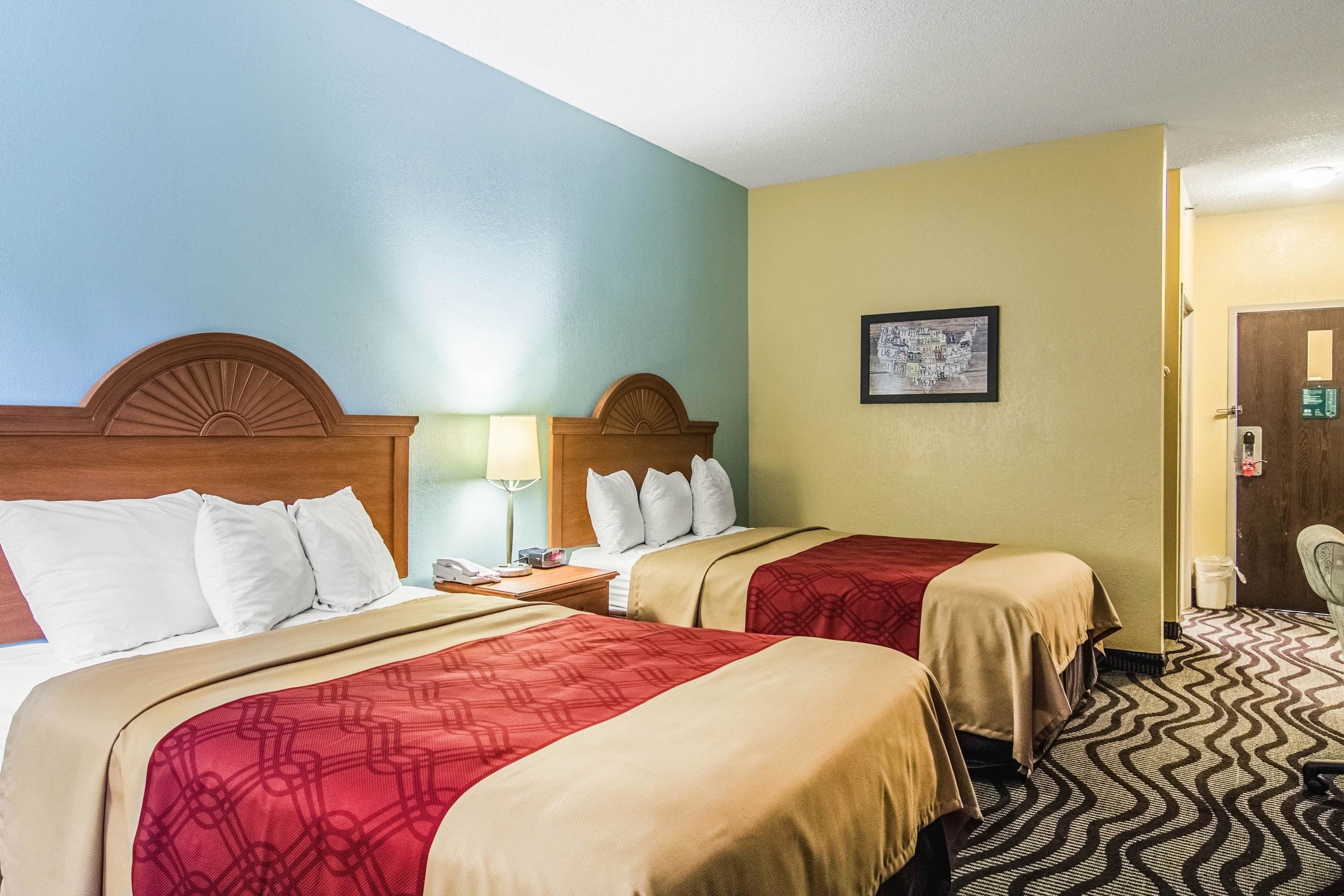 A hotel room with two beds, a wooden headboard, a nightstand with a lamp, and a framed picture on the wall.