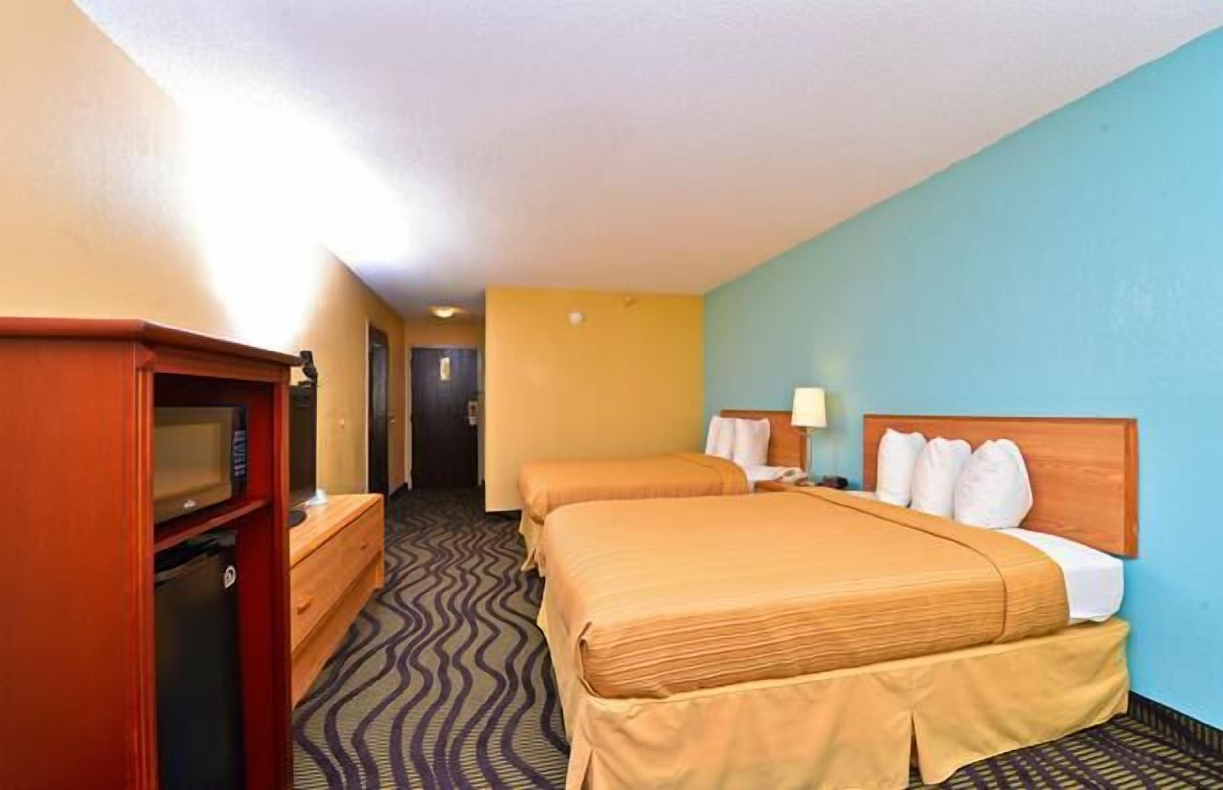 A hotel room with two beds, a desk with a computer, and a microwave.