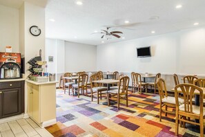 A dining area with wooden chairs and tables, a coffee machine, a clock, and a television on the wall. - Econo Lodge Darien (Darien)