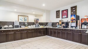 A kitchen with dark brown cabinets, a microwave, toaster, coffee maker, and a coffee station with branded cups and a coffee machine. - Econo Lodge Darien (Darien)