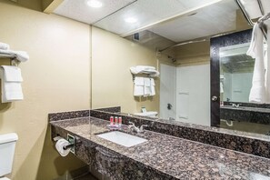 A bathroom with a granite countertop sink, a mirror, and a toilet. - Econo Lodge Darien (Darien)