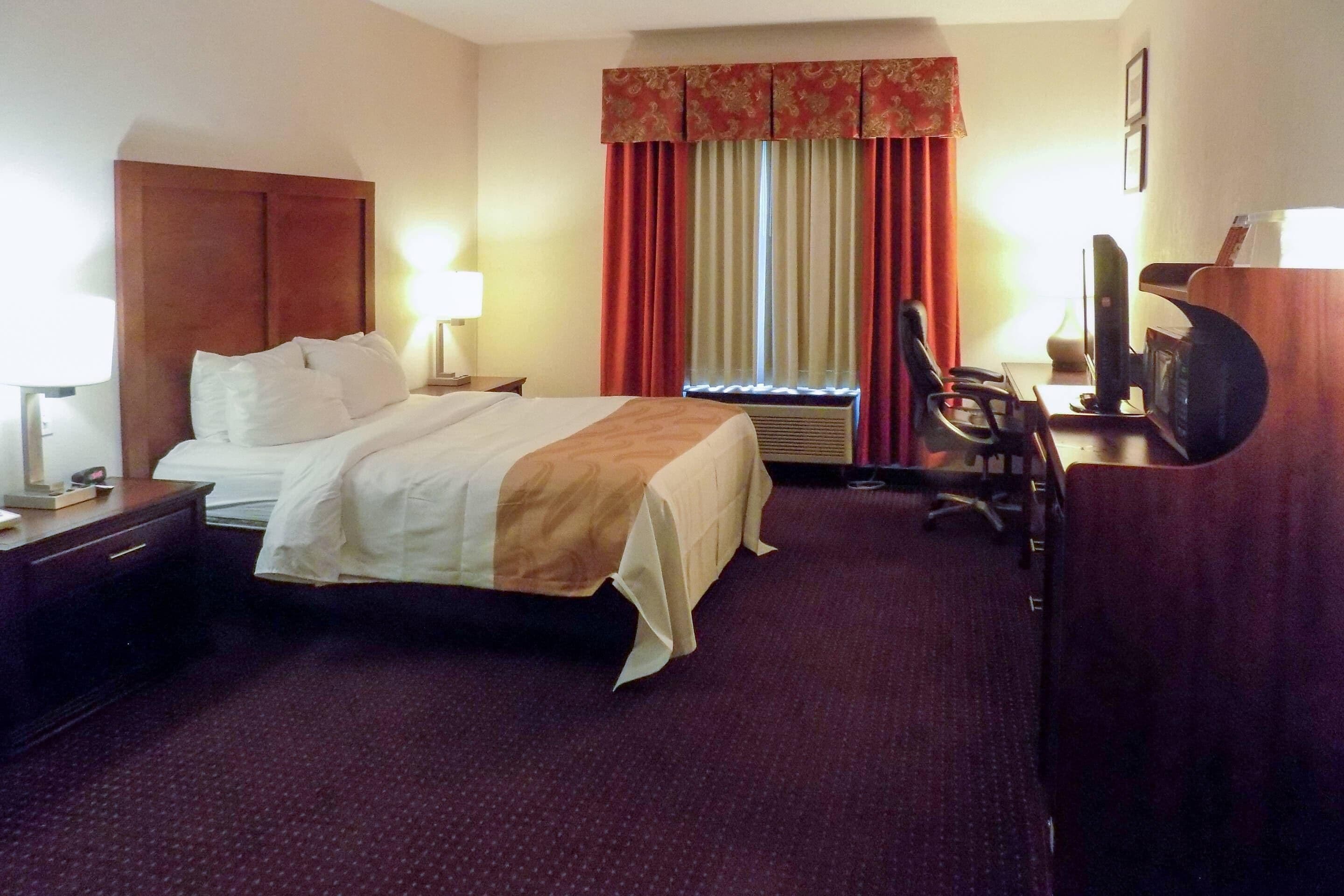 A hotel room with a large bed, a desk with a computer, a chair, and a television.