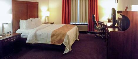 A hotel room with a large bed, a desk with a computer, a chair, and a television.