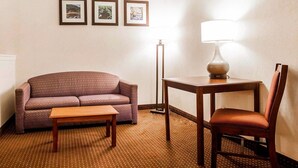 A hotel room with a purple sofa, a wooden table, a lamp, and three framed pictures on the wall. - Quality Inn Kingdom City I-70 (Kingdom City)