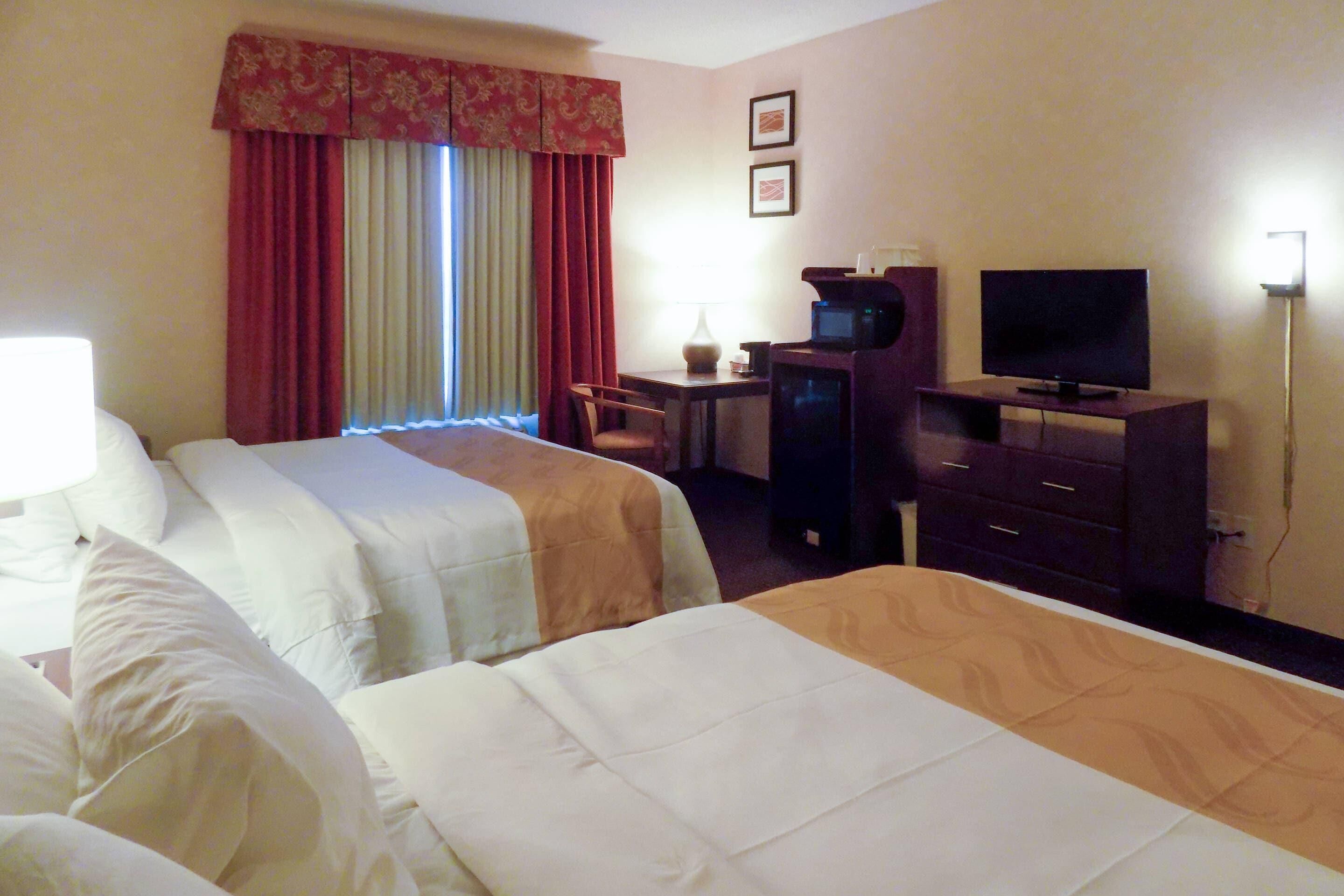 A hotel room with two beds, a desk with a computer, a television, and a lamp.