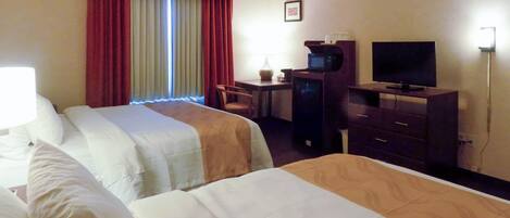 A hotel room with two beds, a desk with a computer, a television, and a lamp.