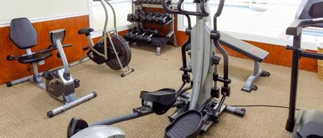 Un gimnasio con diversos equipos de ejercicio, incluyendo cintas de correr, bicicletas estáticas y mancuernas.
